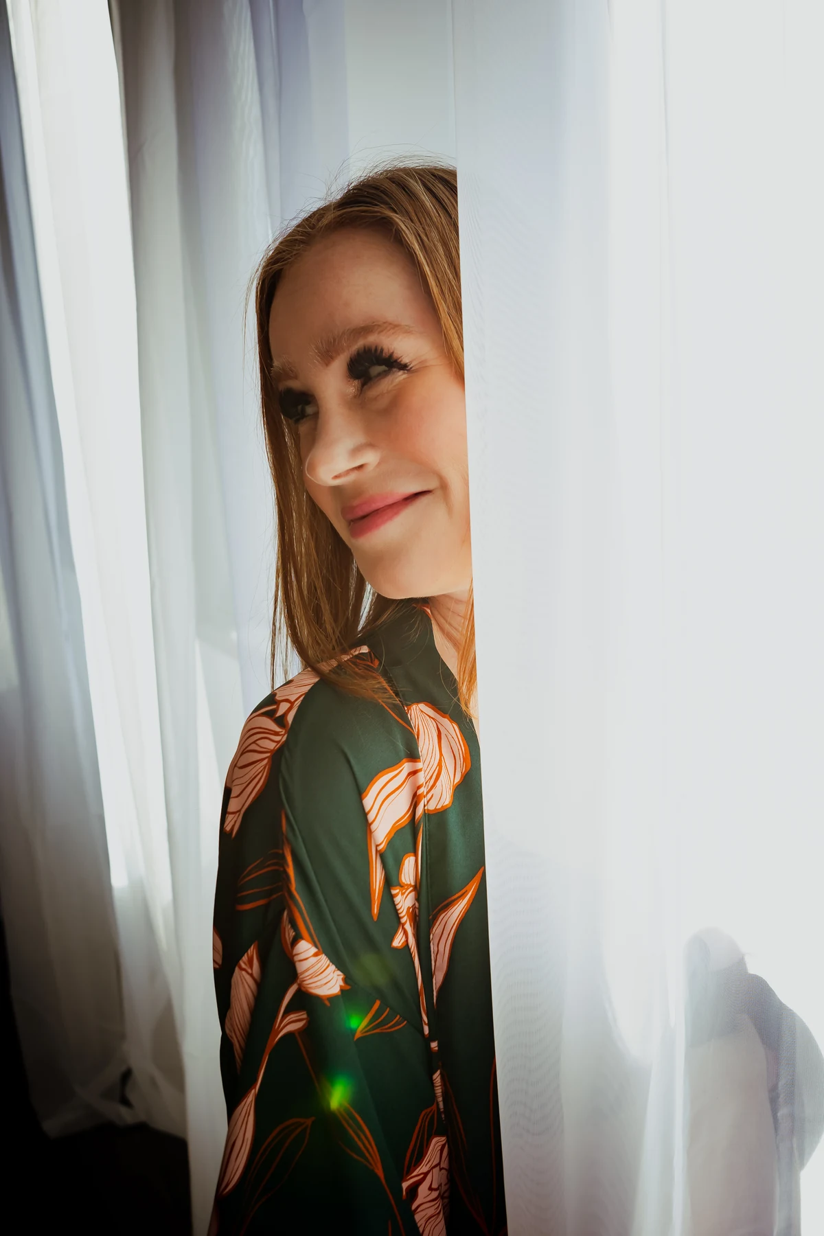 A woman smiling beside the sheer curtains in MKM Photography’s studio.
