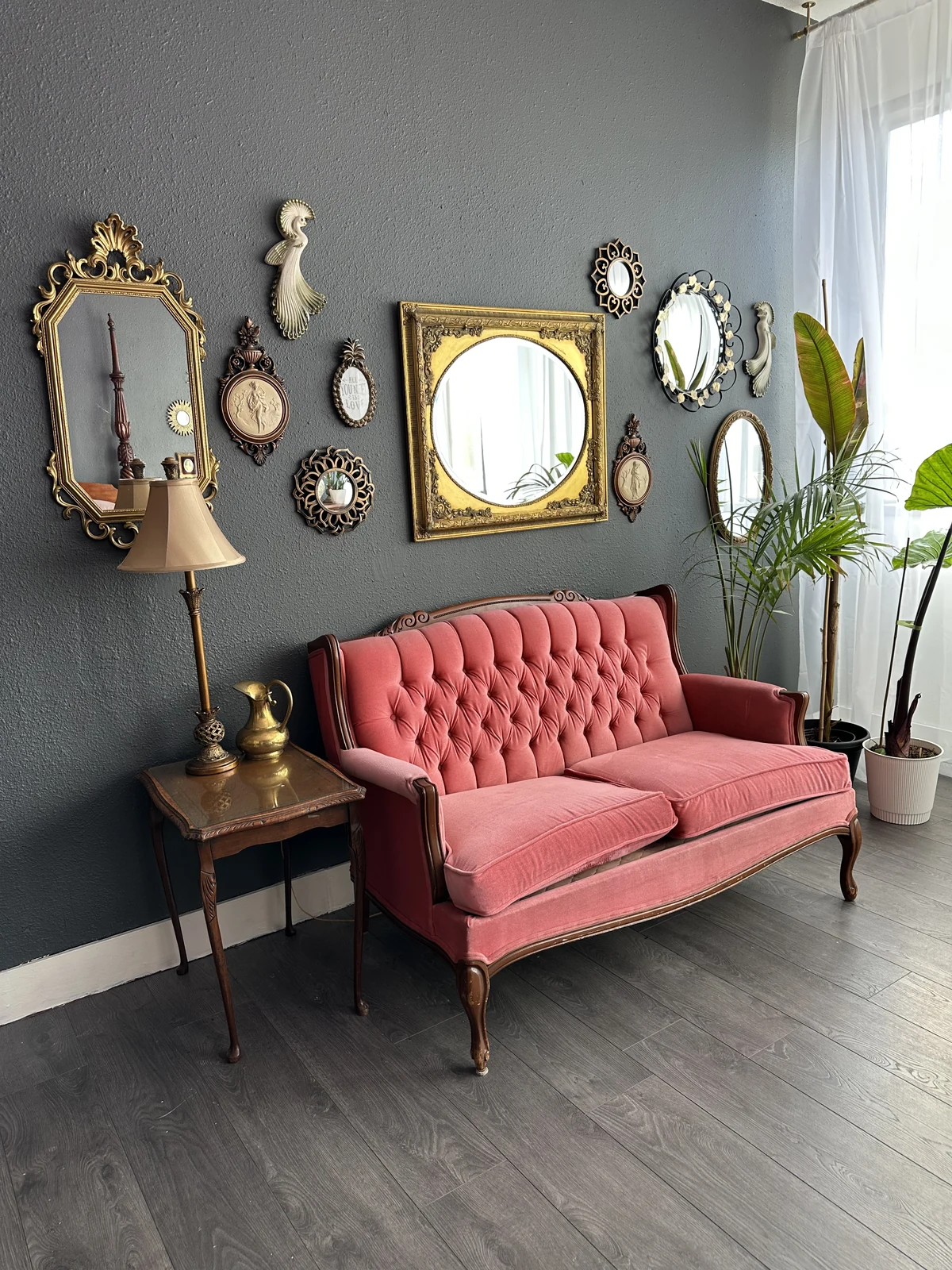 MKM Photography’s studio, with an ornate mirror wall, pink velvet sofa, and plants beside a bright window.
